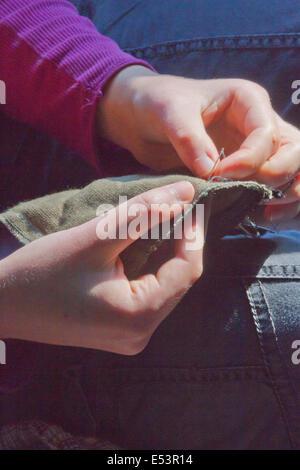 Close up della giovane donna con le mani in mano cucito panno con un ago e filo Foto Stock