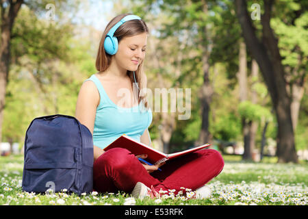 Donna con cuffie che studiano in park seduto sull'erba Foto Stock