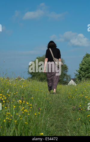Women walking alone through a field with buttercups. Foto Stock