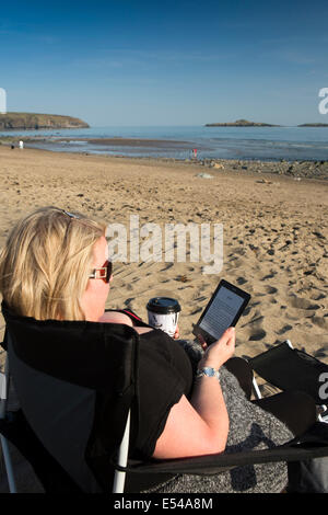 Regno Unito Galles, Gwynedd, Lleyn Peninsula, Aberdaron, spiaggia, donna lettura rilassante libro su ereader di bere il caffè nella luce del sole Foto Stock