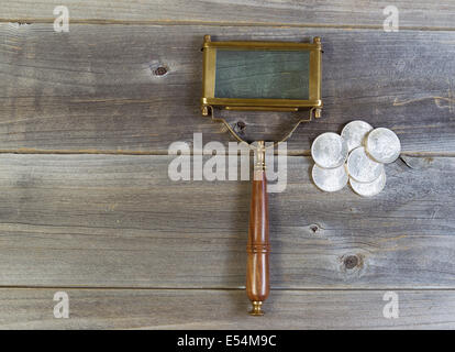 Vista orizzontale di un vecchio di forma rettangolare a forma di lente di ingrandimento e di una pila di vecchi silver dollar monete sul legno rustico Foto Stock