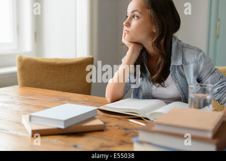 Annoiato studente ragazza seduta home soggiorno che guarda lontano leggere il libro Foto Stock