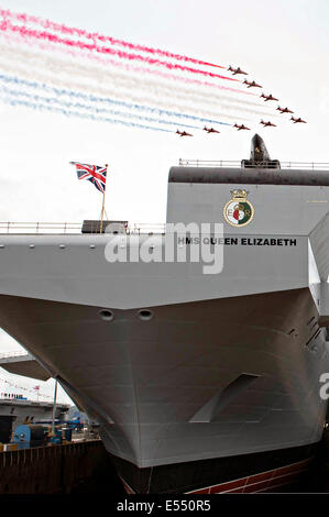 Il Royal Air Force frecce rosse dimostrazione di volo team esegue un cavalcavia della HMS Queen Elizabeth, l'ultima portaerei per la Royal Navy, durante una cerimonia di denominazione presso il cantiere di Rosyth Luglio 4, 2014 a Edimburgo, Scozia. La è la nave di piombo della regina Elisabetta-classe di portaerei, la più grande nave da guerra mai costruita per la Royal Navy e in grado di trasportare fino a un massimo di quaranta aerei. Foto Stock