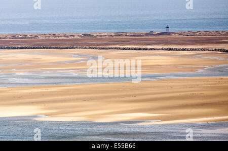 Un faro e una piccola casa sulla spiaggia con l'oceano in vista e la bassa marea e una barriera di pietra in vista. Foto Stock