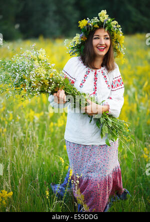 Giovane bella ragazza sorridente in ucraino costume con una corona di fiori alla sua testa in un prato Foto Stock