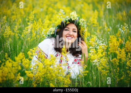 Giovane bella ragazza sorridente in ucraino costume con una corona di fiori alla sua testa in un prato Foto Stock