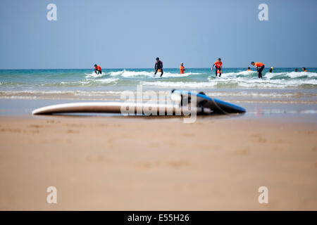 Gruppo di persone aventi lezioni di surf tra le onde su una spiaggia di sabbia in Spagna e tavole da surf in primo piano cielo blu in background Foto Stock