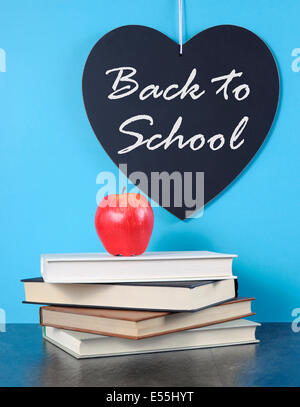 Si torna a scuola cuore lavagna con mela rossa e la pila di libri sul blu con nero ardesia sfondo tabella. Foto Stock