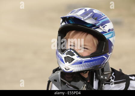 un primo piano di un ragazzo con equipaggiamento protettivo da motocross, incluso un casco, che si prepara a un giro in motocross, mostrando la sua eccitazione e prontezza Foto Stock