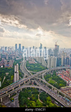 Vista panoramica del traffico delle ore di punta del pomeriggio sull'interscambio della Yanan Express Way con traffico che si attraversa l'un l'altro contro lo skyline della Shanghai occidentale su una nuvola soffusa e insolitamente chiara, cielo blu giorno. Foto Stock