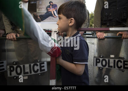 Tehran, Iran. 22 Luglio, 2014. Il governo iraniano ragazzo giovane trattiene l'Iran la bandiera mentre in piedi di fronte a un'immagine di un uomo palestinese e sua figlia come diplomatico le forze di polizia di guardia durante una manifestazione di protesta contro Israele dell azione militare contro la striscia di Gaza, di fronte alla sezione di interessi della Repubblica Araba di Egitto nel nord di Teheran. Manifestanti hanno chiesto in Egitto per riaprire la Rafah Valico di frontiera per il trasferimento di cure mediche a Gaza. Morteza Nikoubazl/ZUMAPRESS Credito: Morteza Nikoubazl/ZUMA filo/Alamy Live News Foto Stock