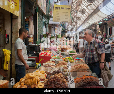 A dried fruit and seeds vendor with shoppers at Machane Yehuda market, Jerusalem, Israel Foto Stock