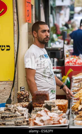 Una di frutta secca, semi, e caramelle venditore in attesa per gli acquirenti a Machane Yehuda Market, Gerusalemme, Israele Foto Stock