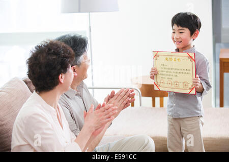 Ragazzo carino che mostra certificato di merito per i nonni Foto Stock