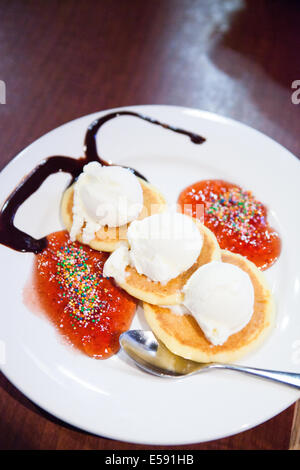 Primo piano della piastra di tre piccole pancake e palline di gelato con confettura di fragole e salsa al cioccolato Foto Stock