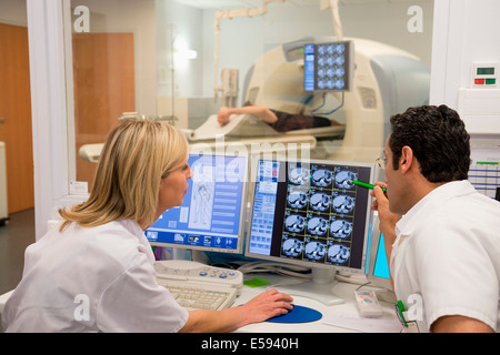 I medici esame di scansione sul computer con il paziente su scanner MRI in background Foto Stock