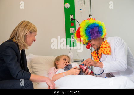 Medico maschio indossando costumi clown rendendo ragazza sorriso del paziente nel letto di ospedale Foto Stock