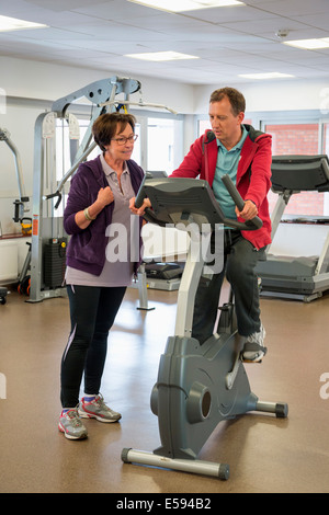 Trainer aiutando una donna con il ciclo in una palestra Foto Stock