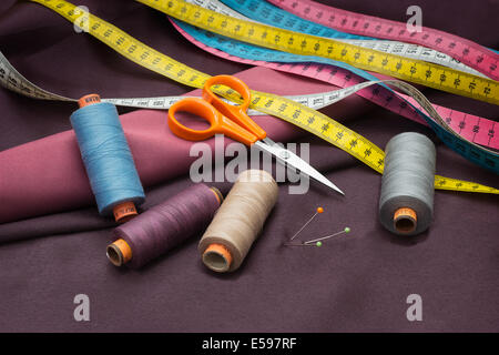Sarti strumenti - bobine di filato pin, forbici e nastro di misurazione sul tessuto rosso. Foto Stock