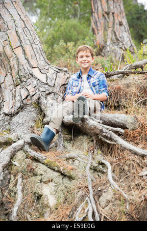 Ragazzo seduto su radici di albero nella foresta Foto Stock