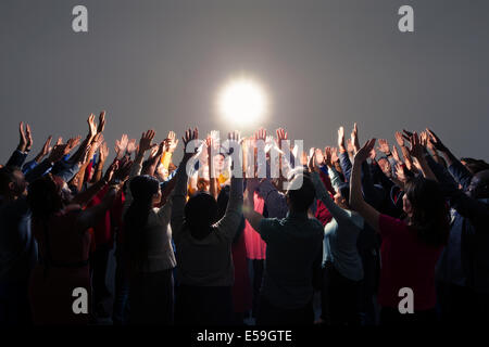 Folla variegata con bracci sollevati intorno a una luce brillante Foto Stock