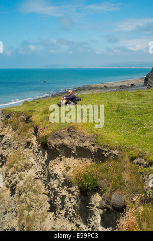 Un viandante si prende una pausa sulla costa del Galles percorso tra Borth e Aberystwyth, Ceredigion, Galles. Foto Stock