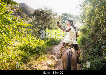 Donna ispanica a scattare foto a cavallo nella giungla Foto Stock