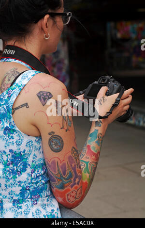 Tatuaggi colorati di copertura braccio womans e vita sulla mano che tiene la fotocamera Canon Foto Stock