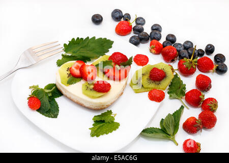 A forma di cuore la cheesecake su piastra bianca decorata con fragole, kiwi e foglie di menta Foto Stock