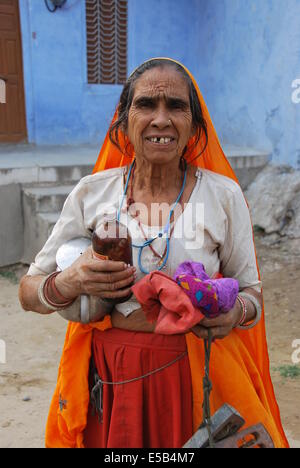 India. Il Rajasthan. Villaggio donna.vestito in arancione . medicina bottiglia. edificio blu dietro. Foto Stock
