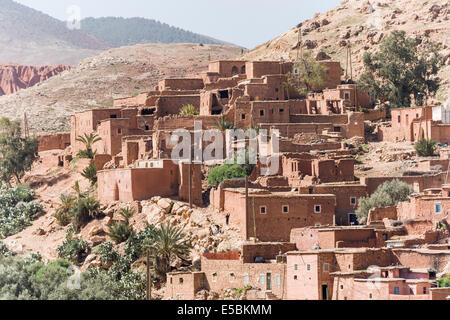 Red case in mattoni, alcuni rovinato, di un villaggio berbero che abbraccia i contorni di una collina in Alto Atlante, Marocco Foto Stock