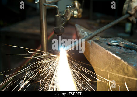 Un costruttore di metallo utilizzando una torcia a calore di un pezzo di metallo per dare forma a. Foto Stock