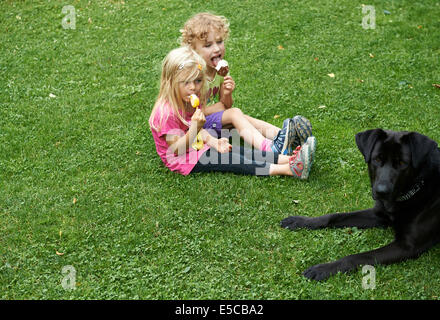 Bambini ragazza bionda mangiare coni gelato seduti sul prato, estate Foto Stock