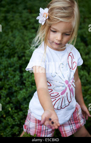 Bambino ragazza bionda di picking e di mangiare mirtilli nella foresta di estate Foto Stock