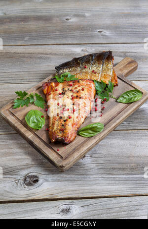 Vista verticale di salmone affumicato filetti, fresco di fornello, con il condimento sulla scheda servente con legno rustico al di sotto Foto Stock