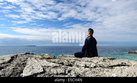Persona la meditazione seduta su una roccia su una riva di un laghetto. La penisola di Bruce, in Ontario, Canada. Foto Stock