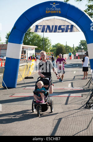 Uomo in 5K o 10K marathon race crossing traguardo con il bambino nel passeggino Foto Stock