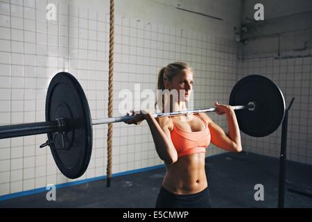 Donna Fitness concentrare durante il sollevamento barbells. Donna forte sollevamento pesi nella palestra crossfit. Caucasian modello femminile con mu Foto Stock