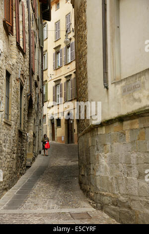 Donna con red shopping bag percorrendo le strette strade di ciottoli, Bergamo Alta, Italia. Foto Stock