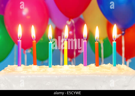 Candele accese su una white iced torta di compleanno con palloncini multicolori in background, spazio copia sulla torta per aggiungere la vostra Foto Stock