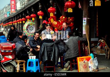 JUN LE CITTÀ, Cina: un gruppo di uomini a giocare a carte di fronte a un negozio con righe di tessuto rosso lanterne per l'Anno Nuovo Cinese Foto Stock