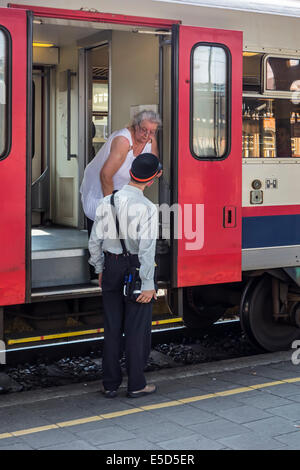 Anziani passeggero femmina chiedendo informazioni al dipendente ferroviario / ticket inspector da treno su piattaforma in stazione ferroviaria Foto Stock