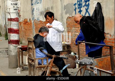 Il jiu CHI TOWN, CINA: Barbiere dando un client un taglio di capelli nel suo outdoor Barber shop Foto Stock