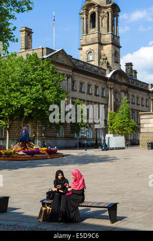 Due giovani ragazze musulmane in abito tradizionale seduti di fronte al Municipio, la piazza del mercato, Preston, Lancashire, Regno Unito Foto Stock