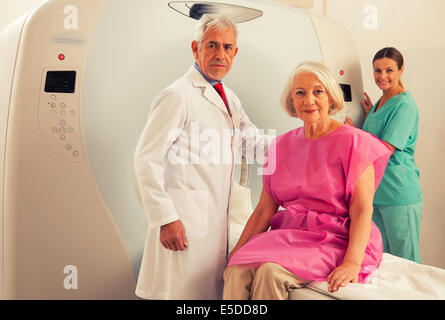 Donna in 60s pronto per essere controllato sotto scanner MRI con i senior medico e sorridente assistente femmina. Foto Stock