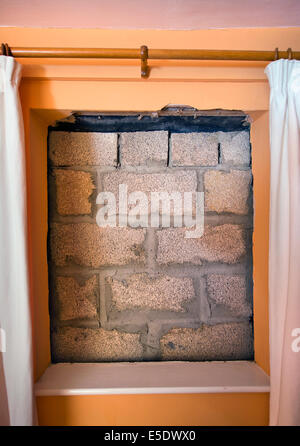 Una finestra murata con blocchi in calcestruzzo con camera da letto tende ancora appeso Foto Stock