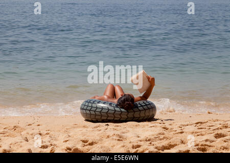 Una donna il relax e la lettura di un libro sulla spiaggia nel periodo delle vacanze estive, Algarve, Portogallo Europa Foto Stock