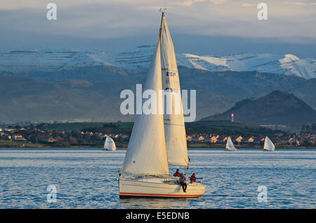 Barche a vela al tramonto sulla baia di Santander. Sullo sfondo le montagne coperte di neve del Cantabrico gamma può essere visto. Foto Stock