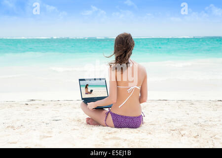 Una giovane donna che utilizza un computer lap top sulla spiaggia del Mar dei Caraibi Foto Stock
