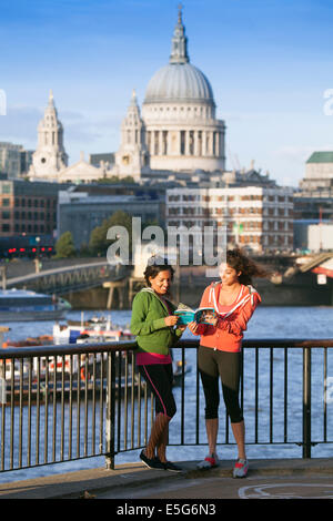 Due giovani DONNE CHE guardano insieme un libro sulla riva sud del Tamigi, Londra, Inghilterra, Regno Unito Foto Stock